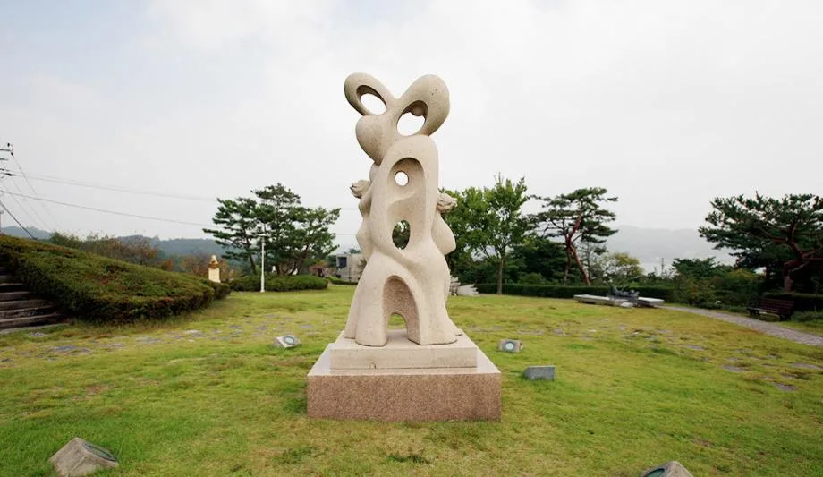 예당호 조각공원 내 석조 조형물과 잔디광장, 뒤편 저수지와 산자락이 보이는 풍경